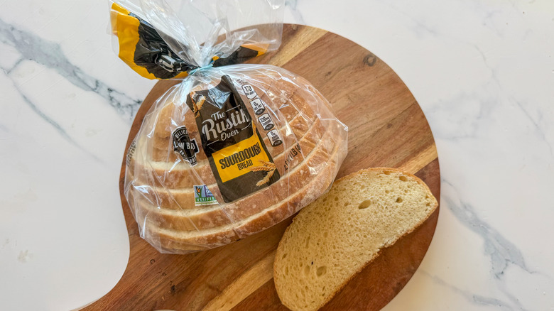 The Rustik Oven sourdough bread in package with a slice on a wooden cutting board