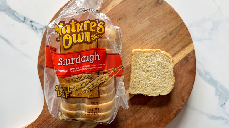 Nature's Own sourdough loaf in wrapper with slice on cutting board