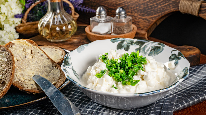 A bowl of cottage cheese topped with herbs, next to bread.