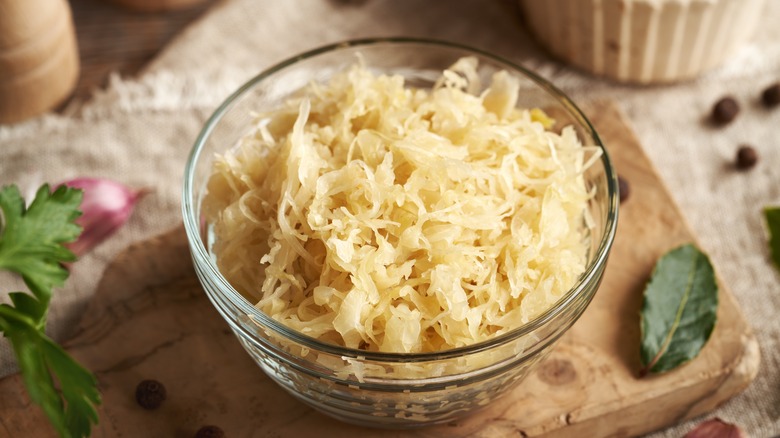 A glass bowl of sauerkraut on a cutting board.