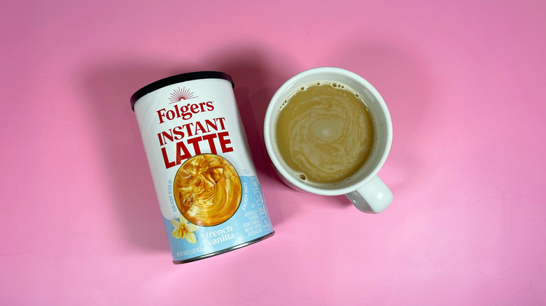 A container of Folger's instant latte mix next to a mug