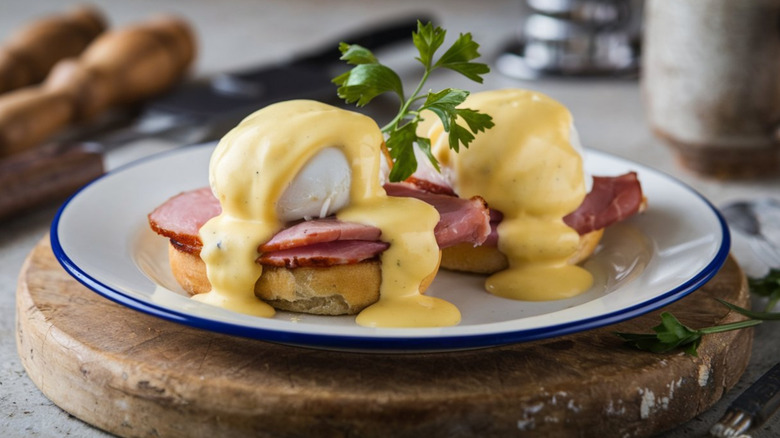 A plate of eggs Benedict on top of a wooden board