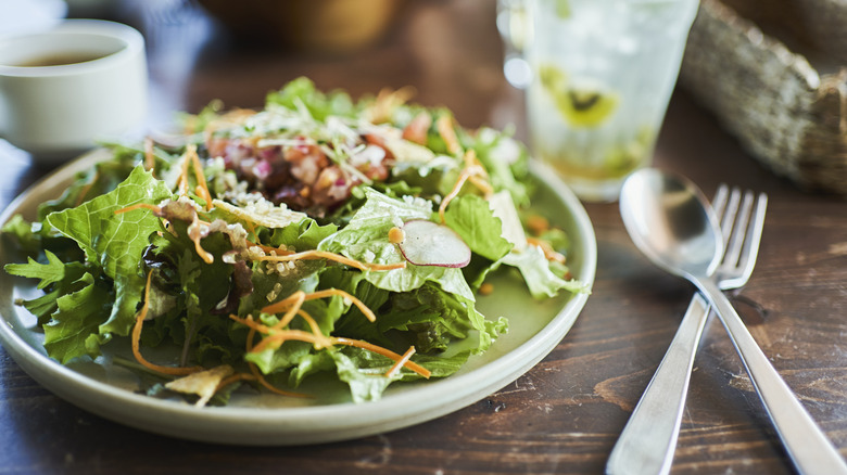 A salad next to silverware on a diner table