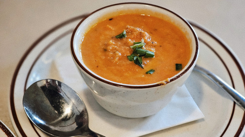 A cup of orange-colored soup on a plate with a spoon