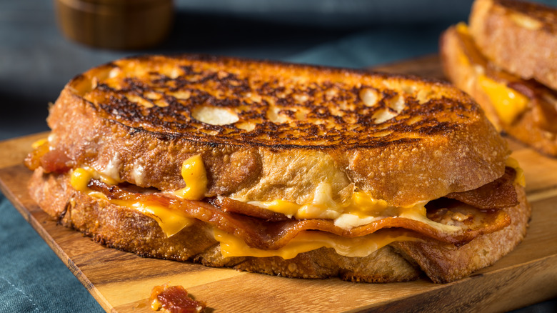 a grilled cheese with bacon sitting on a cutting board