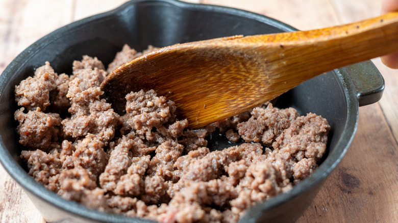 wooden spoon stirring ground beef in a cast iron pan