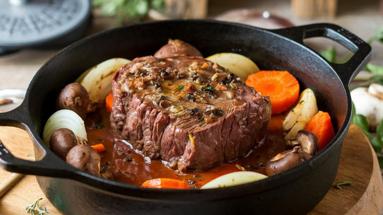 pot roast in center of a cast iron Dutch oven with carrots, mushrooms, and onions