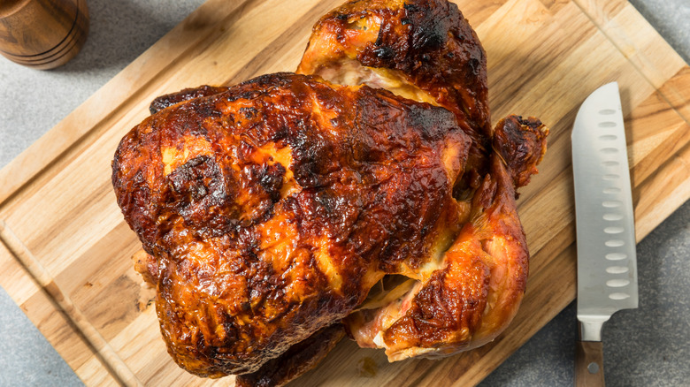 cooked rotisserie chicken on cutting board beside a santoku knife