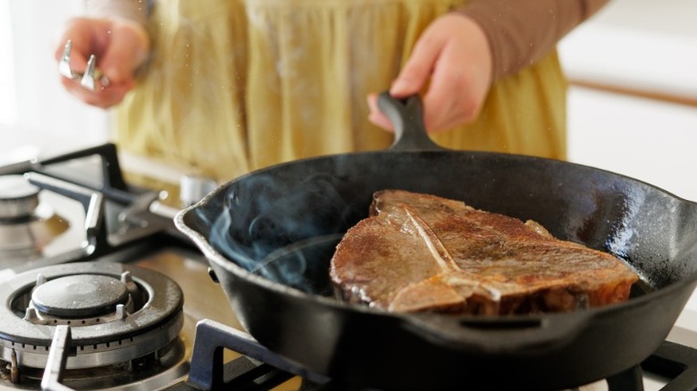 A large cut of meat being seared in a cast iron skillet