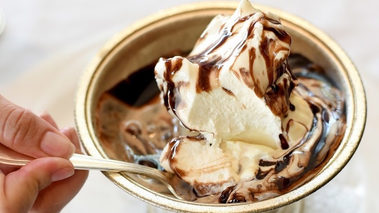 A person taking a scoop of a hot fudge sundae