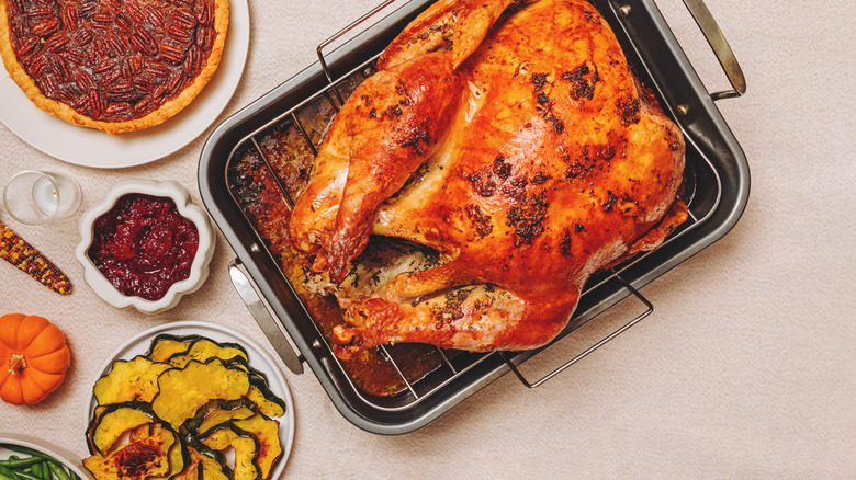 Roast turkey in a roasting dish, surrounded by classic Thanksgiving accompaniments