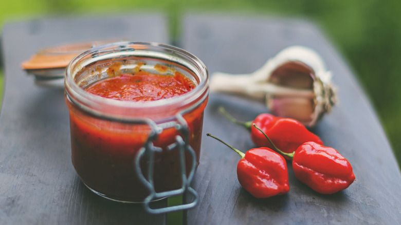 A jar of chili paste on a gray slab next to fresh chili peppers