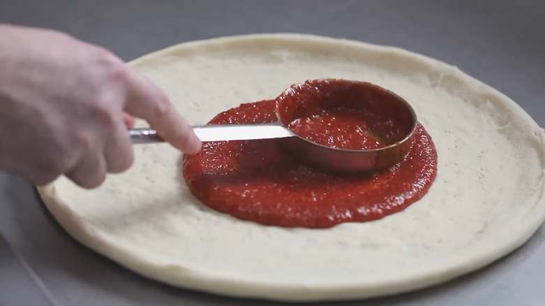 Person spreading red sauce on pizza dough