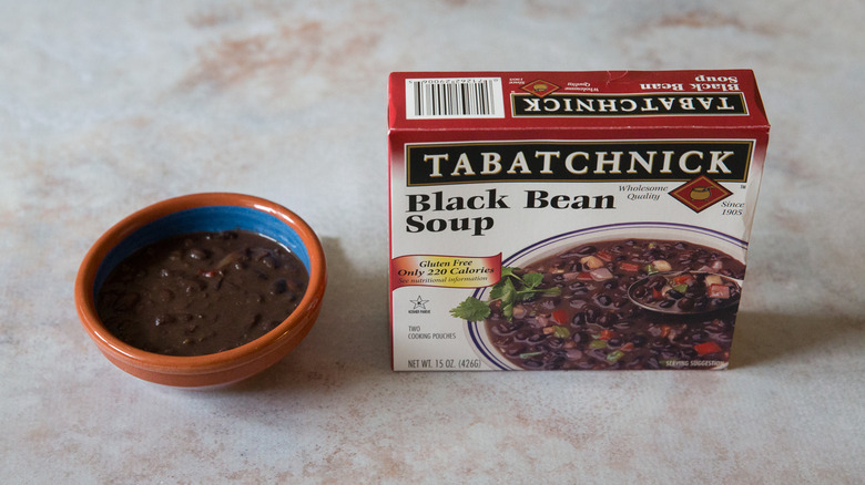 A black bean soup tasting bowl and package are sitting on a pink marble table.