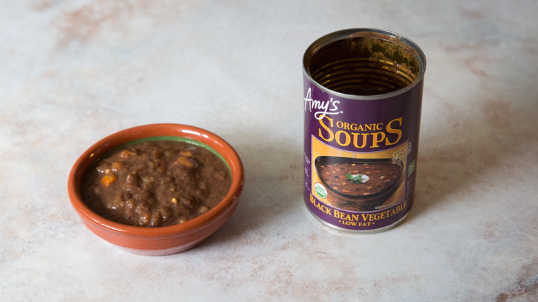 A black bean soup tasting bowl and package are sitting on a pink marble table.