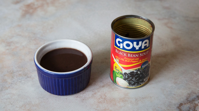 A black bean soup tasting bowl and package are sitting on a pink marble table.