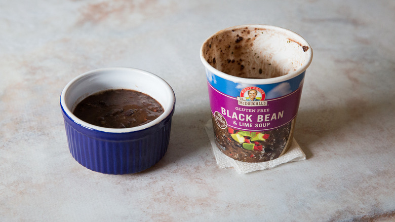 A black bean soup tasting bowl and package are sitting on a pink marble table.