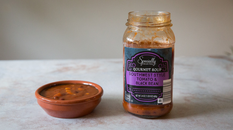 A black bean soup tasting bowl and package are sitting on a pink marble table.