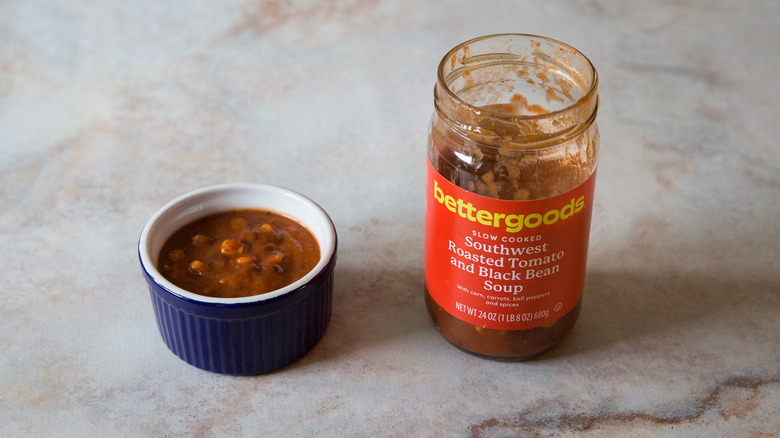 A black bean soup tasting bowl and package are sitting on a pink marble table.