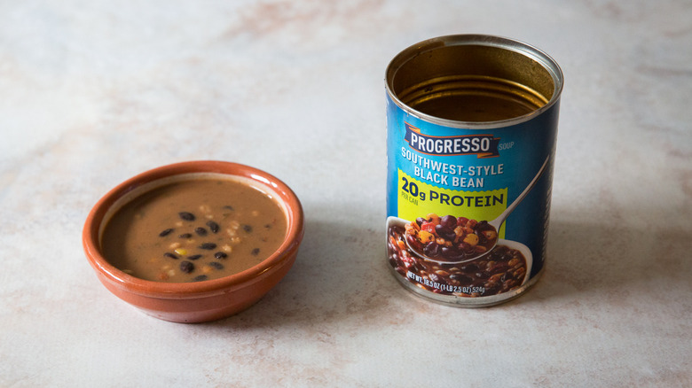 A black bean soup tasting bowl and package are sitting on a pink marble table.