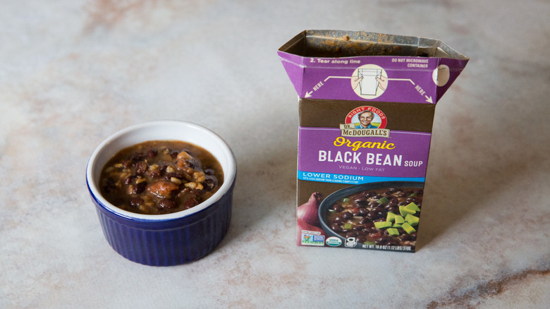 A black bean soup tasting bowl and package are sitting on a pink marble table.