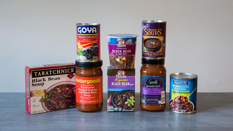 Eight assorted store-bought black bean soups are arranged on a table.