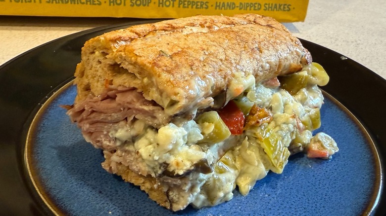 A roast beef and bleu cheese sandwich with toppings on a black and blue plate
