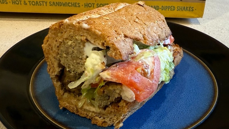 A meatball sandwich with tomato, lettuce, and mayo on a black and blue plate