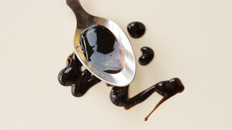 A spoonful and drizzle of balsamic vinegar on a white background