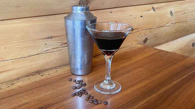 A cocktail shaker and an espresso martini in a martini glass