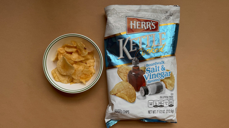Bag and bowl of Herr's Kettle Cooked Boardwalk Salt & Vinegar Chips on brown surface