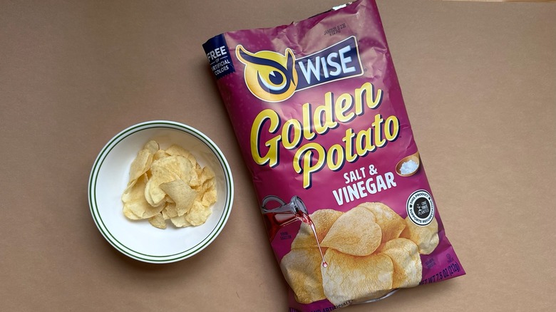 Bag and bowl of Wise Golden Potato Salt & Vinegar Chips on brown surface