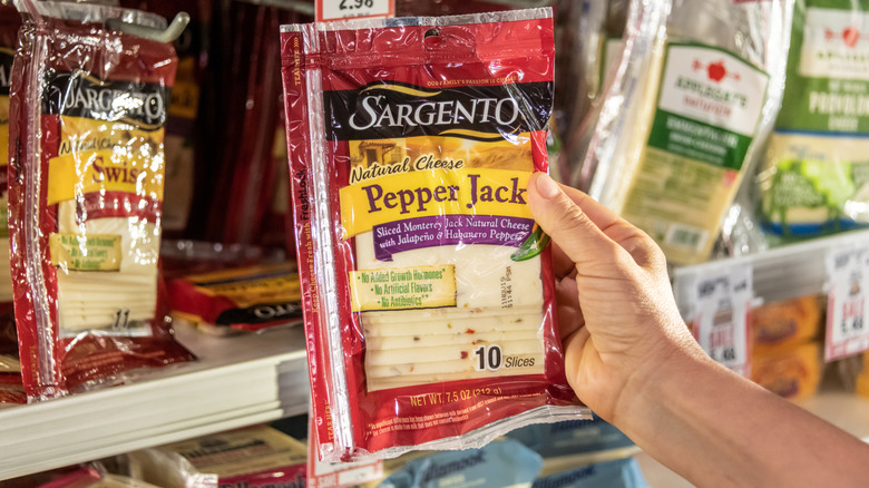 A hand holding a pack of Sargento Pepper Jack Cheese in a supermarket.