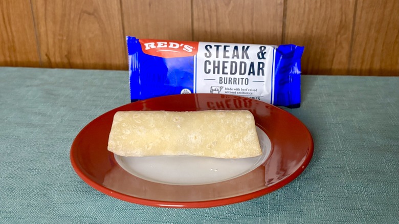 Red's Steak & Cheddar Burrito on a red plate, in front of the burrito's packaging