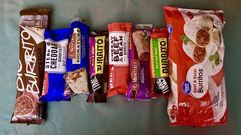 A row of frozen microwavable burritos - from left Tina's Big Burrito Beef & Bean, Red's Steak & Cheddar, El Monterey's Signature Shredded Steak and Cheese, Tina's Beef & Bean, Red's Cheesy Beef & Bean, El Monterey's Beef and Bean, Tina's Red Hot Beef Burrito, and a value pack of 8 Great Value Beef & Bean burritos