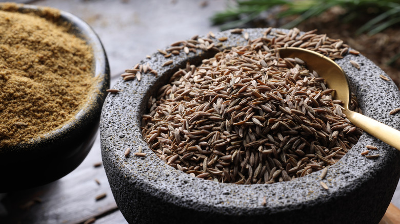 A mortar full of cumin seeds with spoon