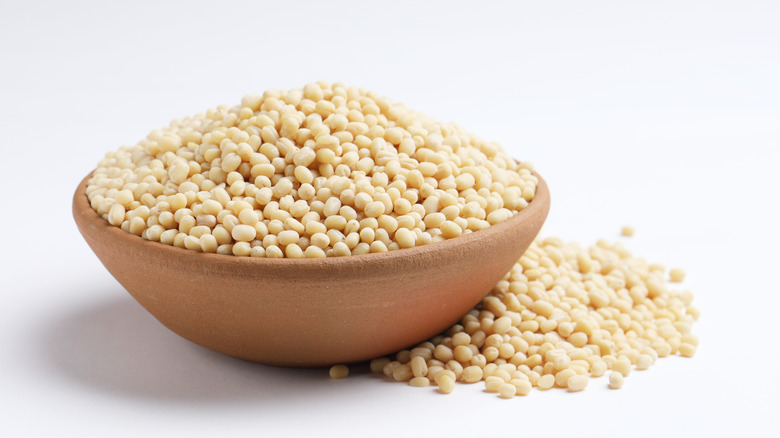 A wood bowl full of white urad dal with some on surface next to the bowl