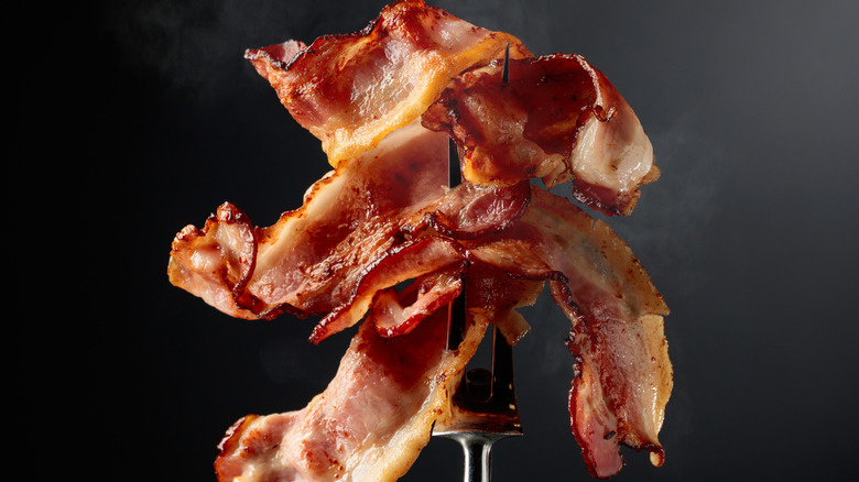 Several strips of bacon on a fork on a black background