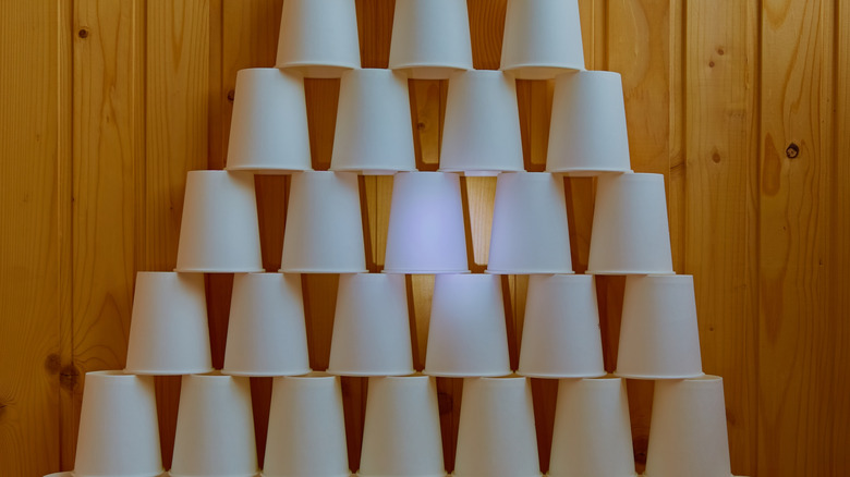 A pyramid of white paper cups against a wood-paneled wall