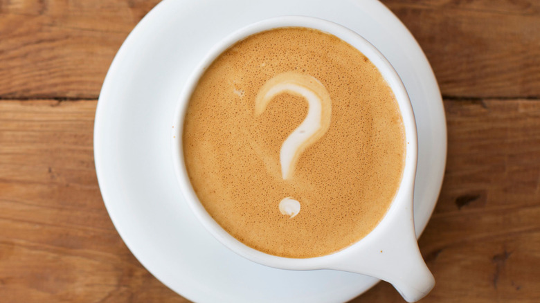 Top view of a coffee cup on a wood table, with a question mark in foam on the coffee's surface