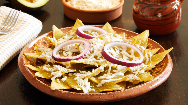 A plate of chilaquiles with salsa verde, queso fresco, crema, and red onions
