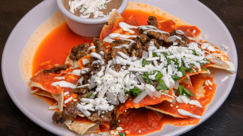A plate of chilaquiles with salsa roja, carne asada, and garnishes