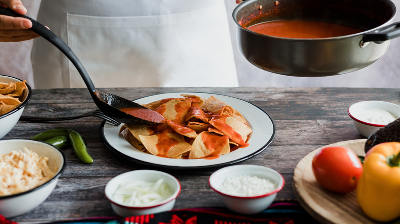 A woman adding salsa to chilaquiles