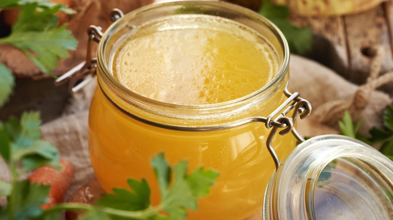 Chicken broth in a canister surrounded by herbs