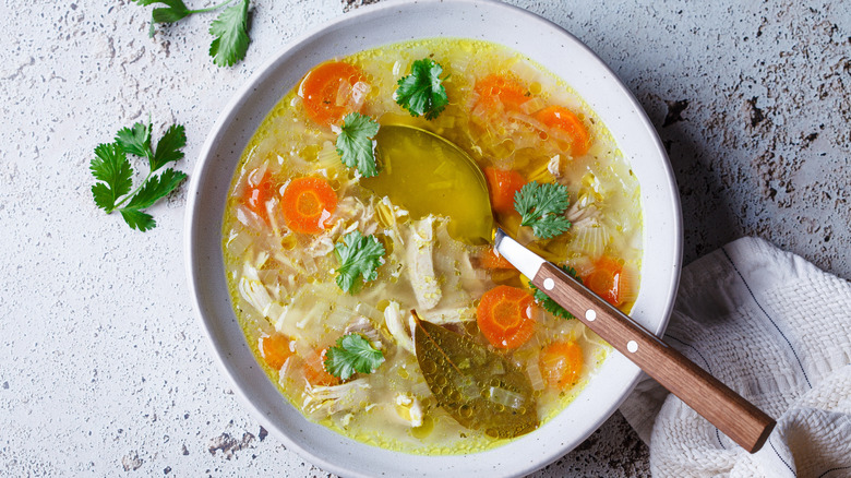 A bowl of chicken soup with vegetables and fresh herbs and a spoon