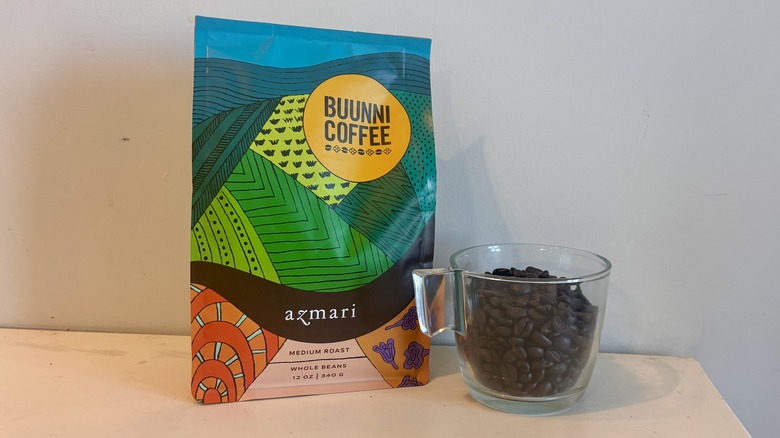 bag of Trader Joe's coffee sitting next to a glass mug of coffee beans on a counter