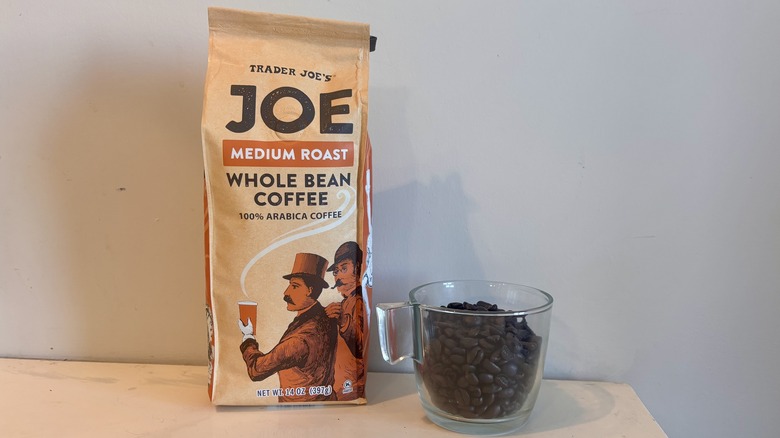 bag of Trader Joe's coffee sitting next to a glass mug of coffee beans on a counter
