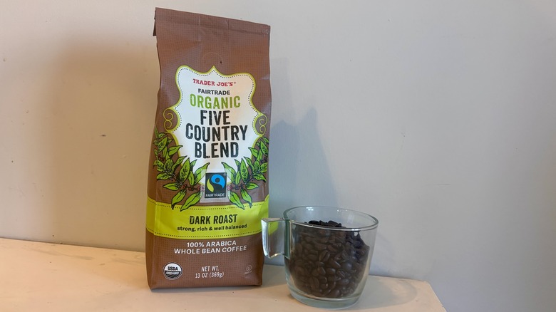 bag of Trader Joe's coffee sitting next to a glass mug of coffee beans on a counter