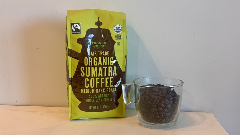 bag of Trader Joe's coffee sitting next to a glass mug of coffee beans on a counter