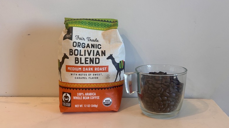 bag of Trader Joe's coffee sitting next to a glass mug of coffee beans on a counter